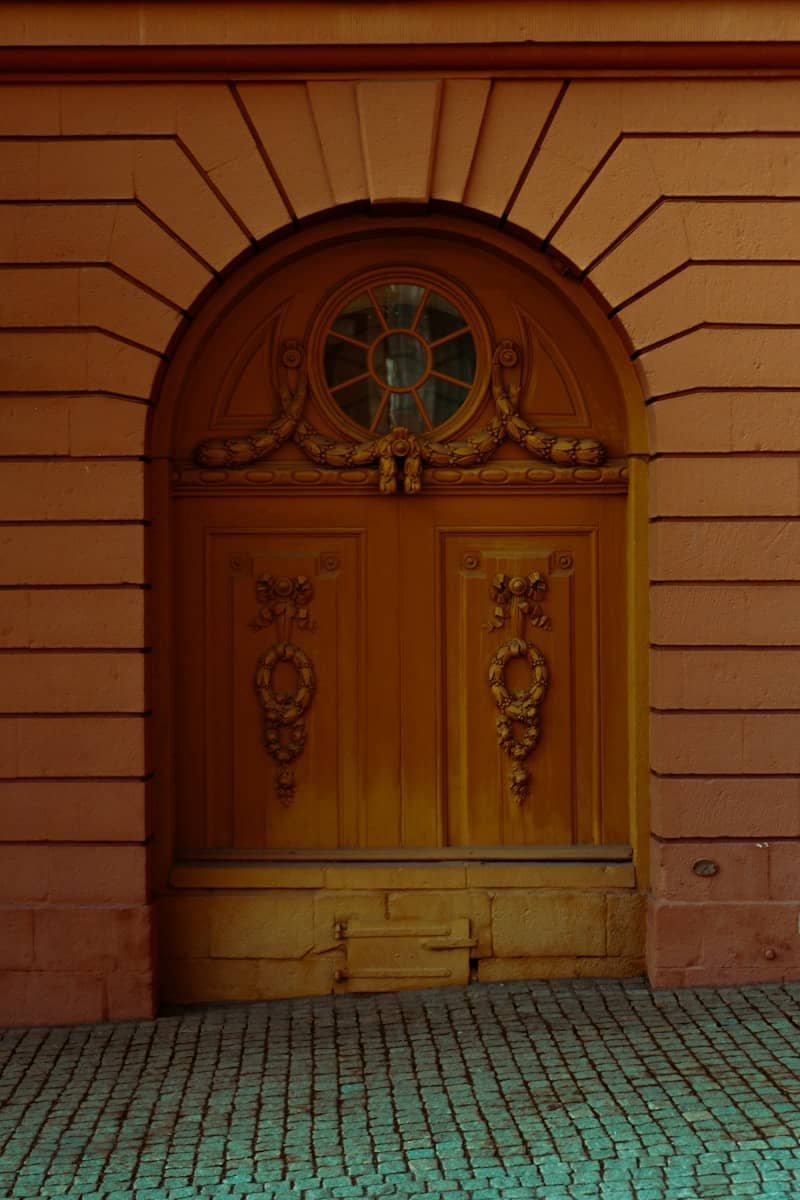 An ornate, arched wooden door stands in a brick wall.