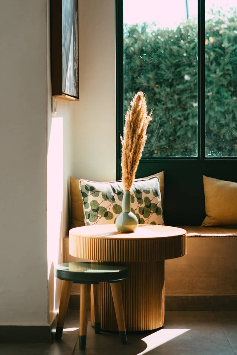 A vase of grass sits on a wooden table.