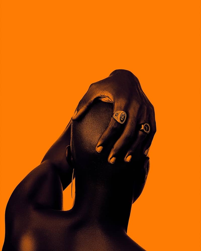Dark silhouette of a person's head with hand against orange