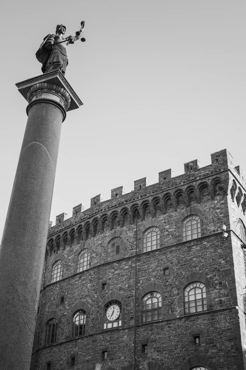 A statue of Justice atop a tall stone column beside a medieval stone building