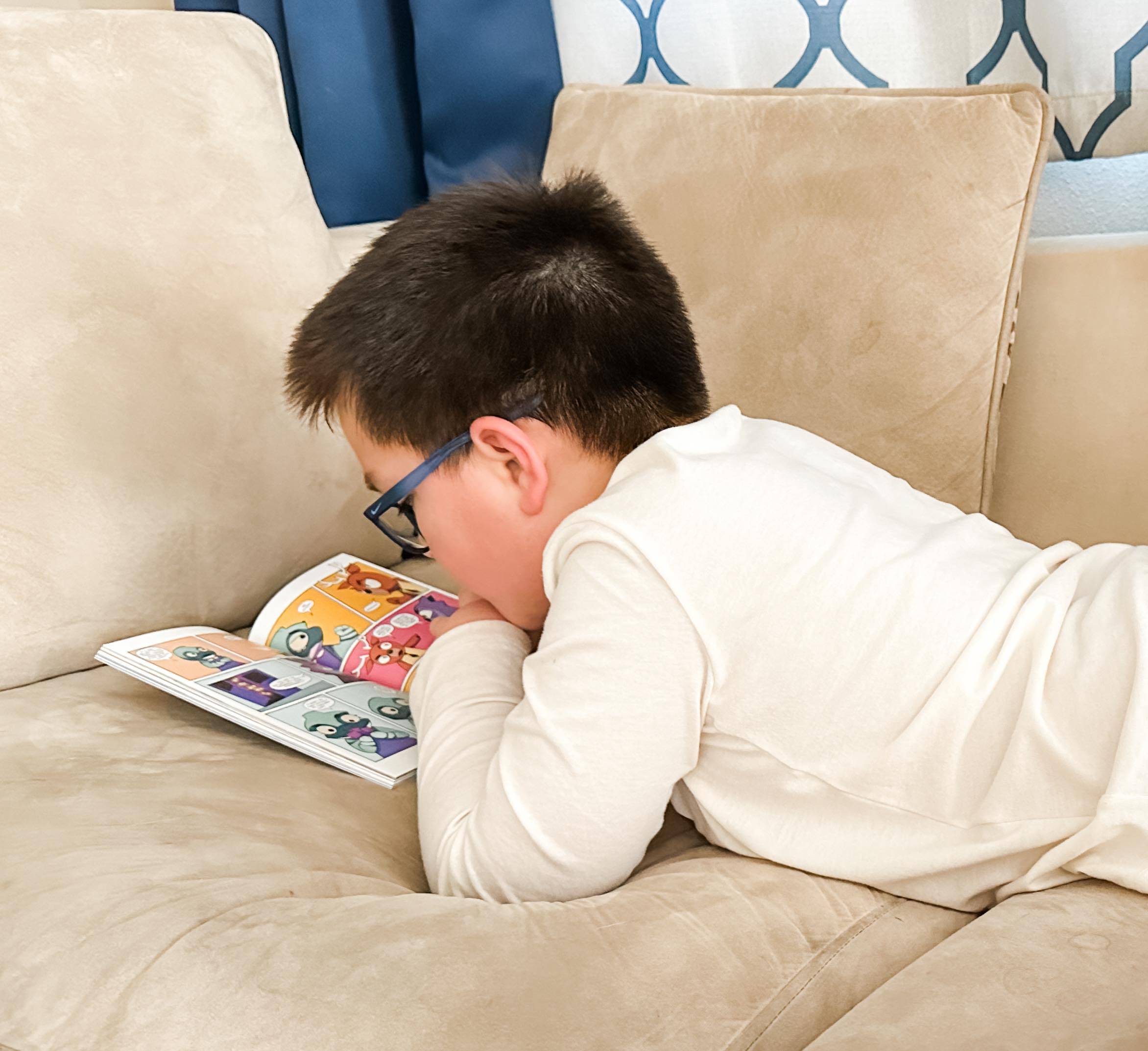 Young boy reading a book on the couch at home