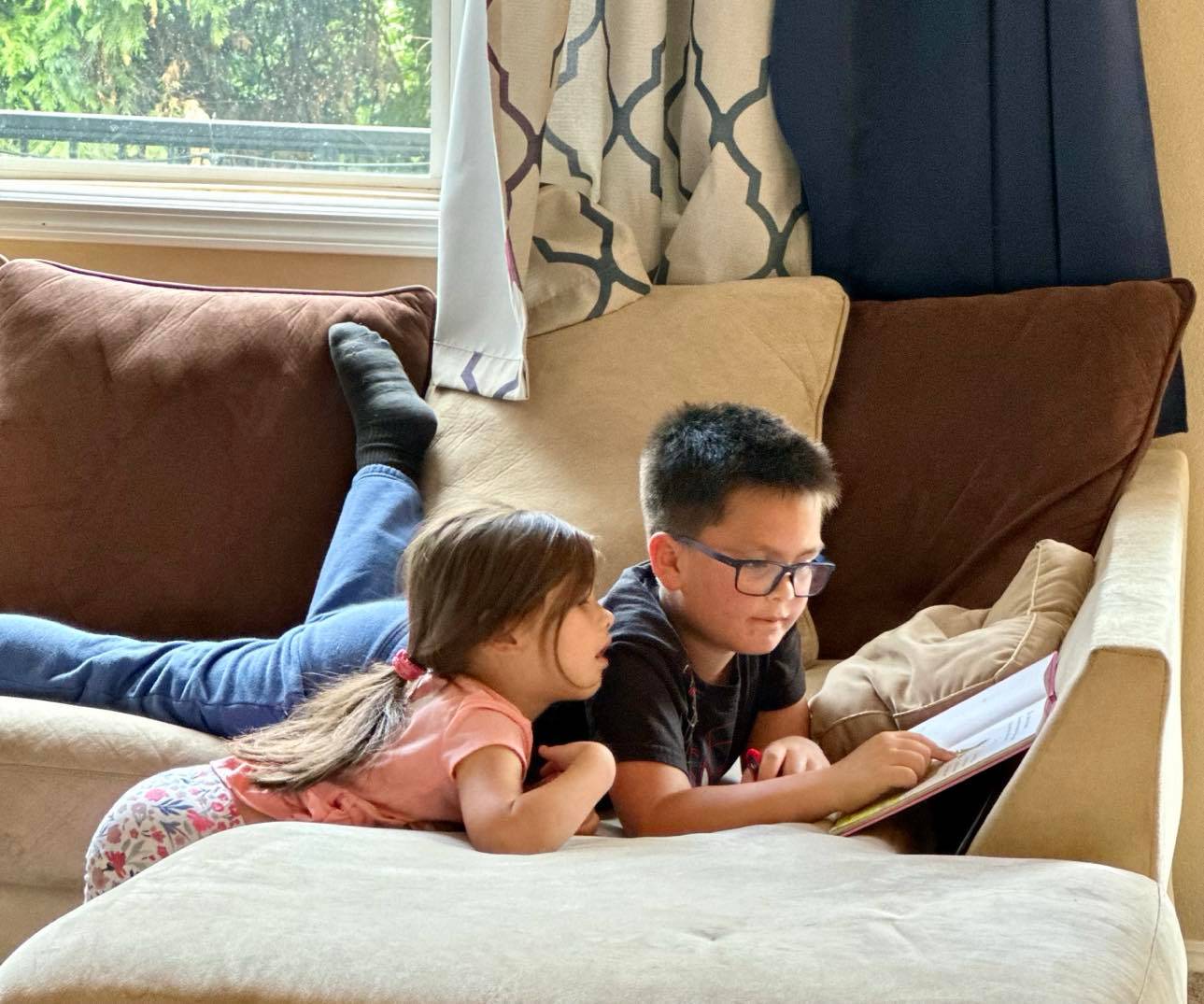 Young boy reading a book to his little sister