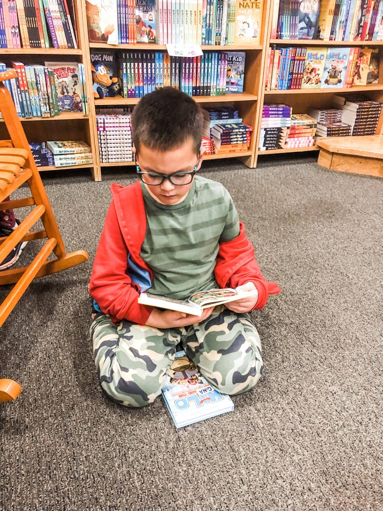 Young boy sitting on the floor of a bookstore reading a book