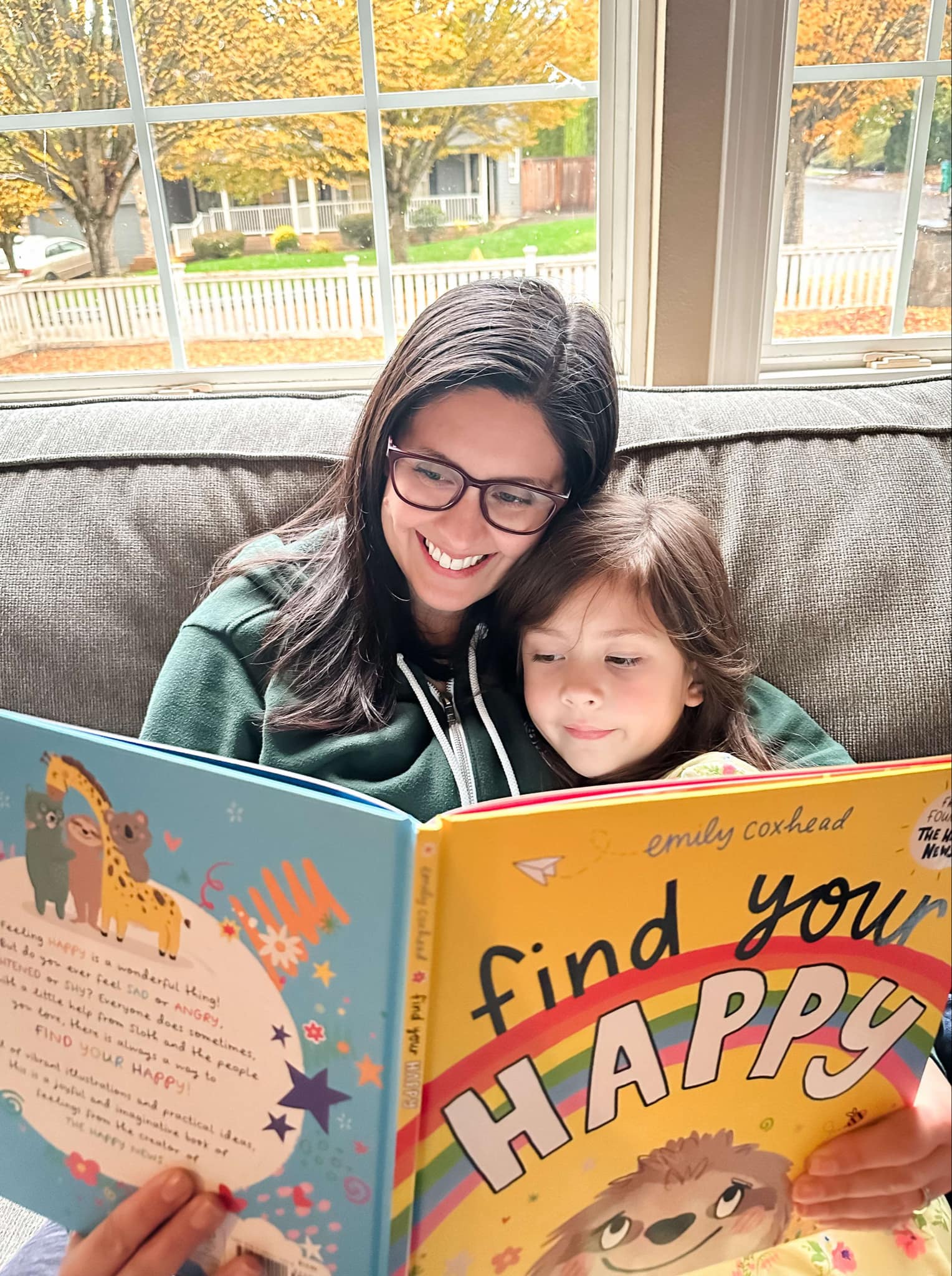 mother and young daughter on the couch reading a book entitled Find Your Happy