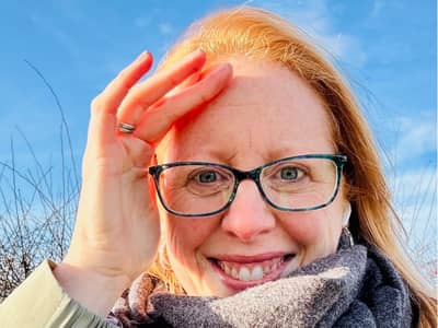 A red haired woman in glasses looking at the camera