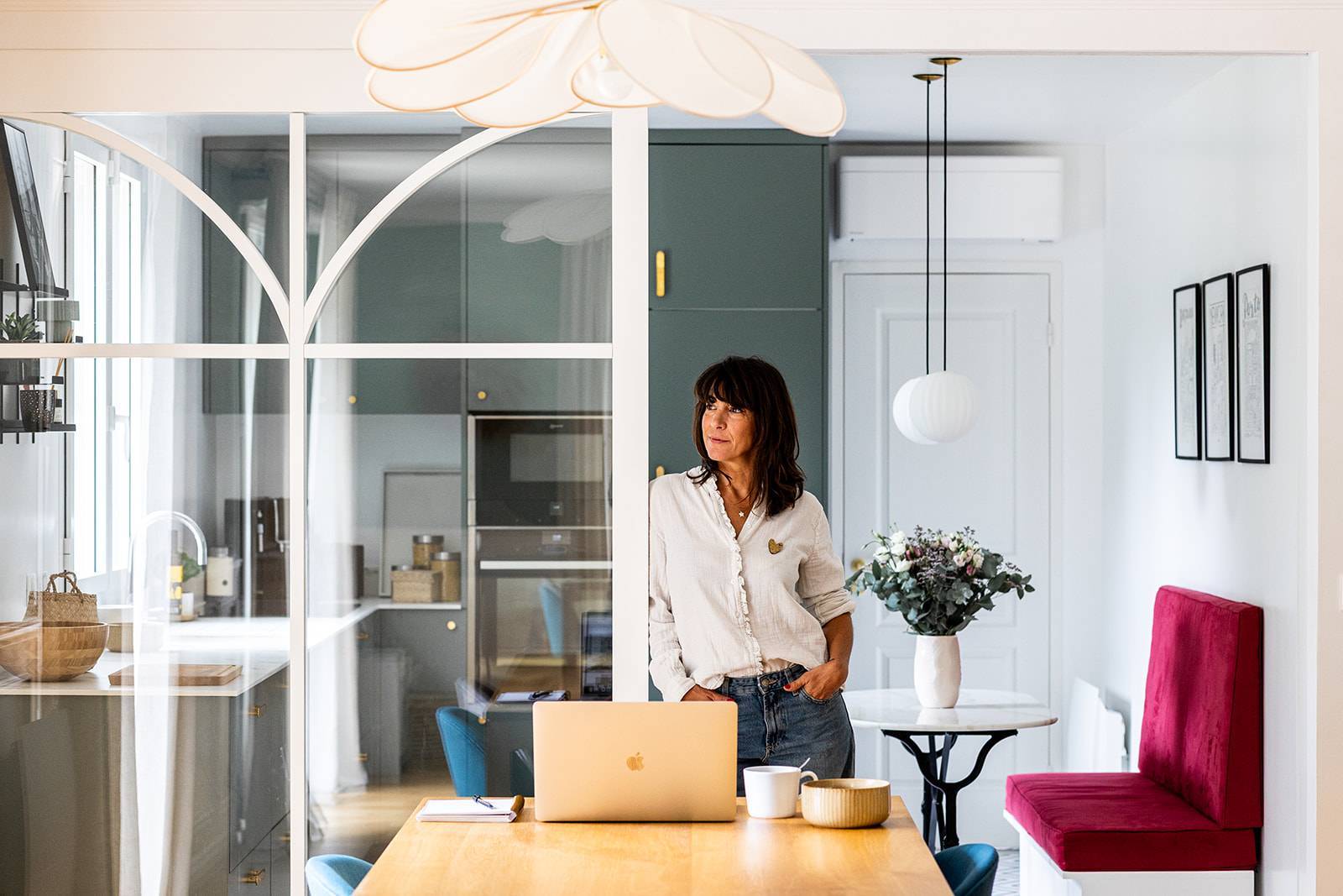 Architecte d’intérieur debout derrière une table en bois avec ordinateur portable, dans un intérieur lumineux et contemporain.