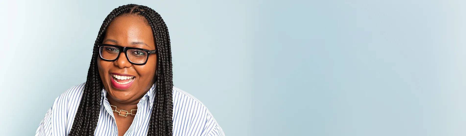 Woman with braids and glasses smiling against a light blue background.