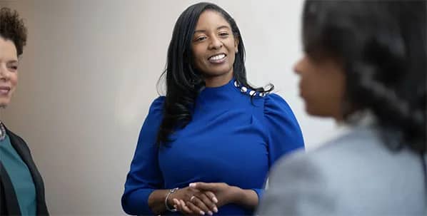 Professional Black woman in a blue dress confidently engaging in conversation.