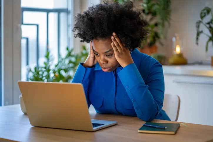 Woman holds head in frustration while working on laptop at home