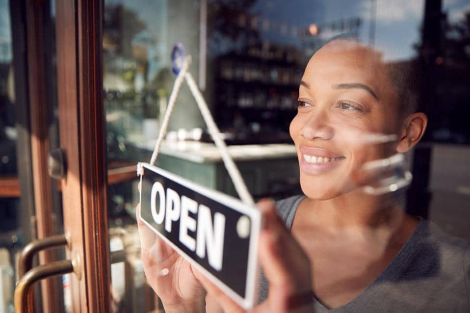 Woman hangs open sign while starting her business day