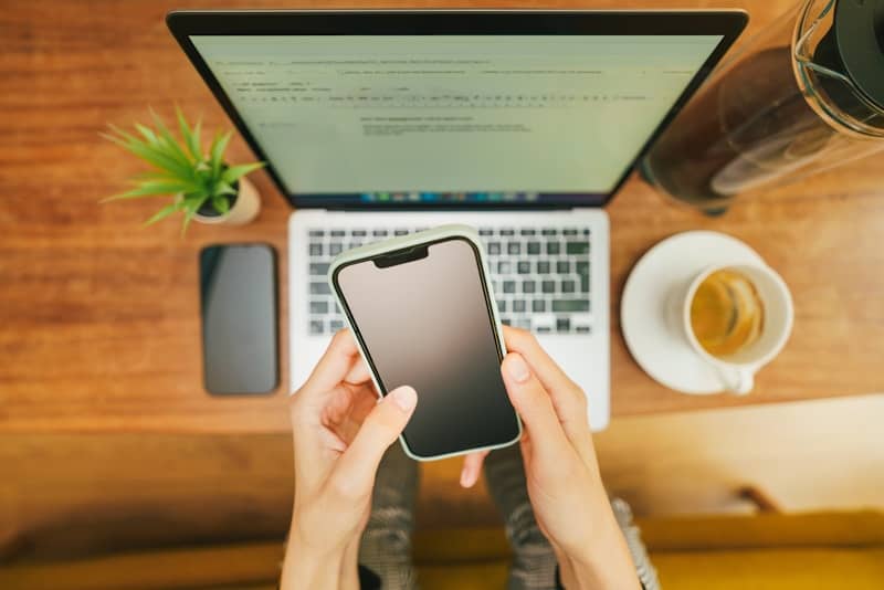 A person holding a cell phone in front of a laptop