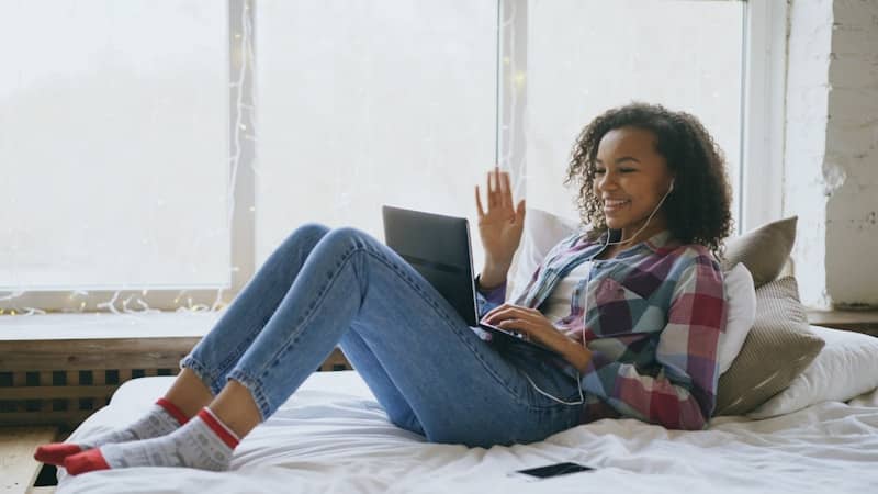 Young woman waves while video calling on laptop.