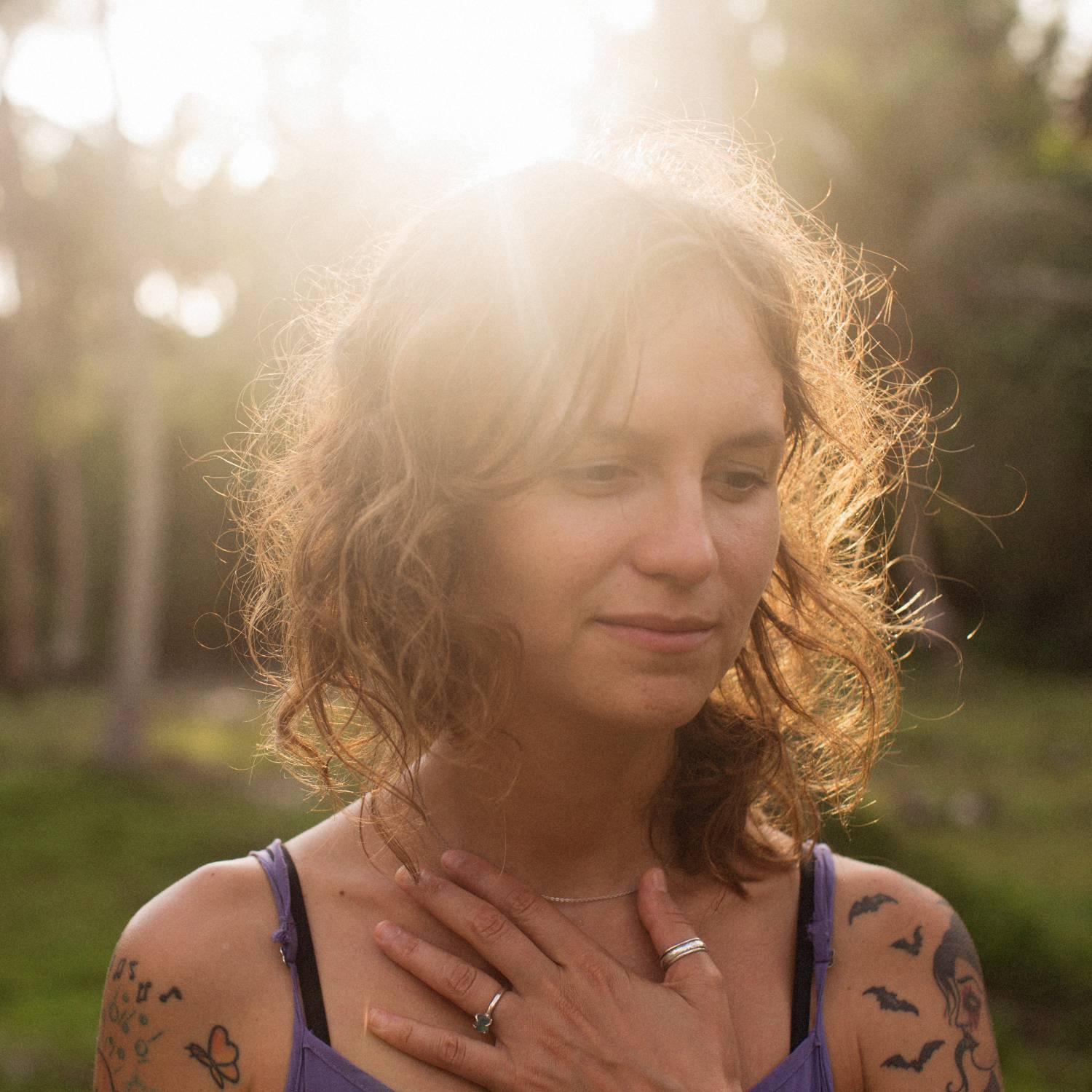 a white woman with brown hair has her hand placed over her heart and the sun shining just overhead