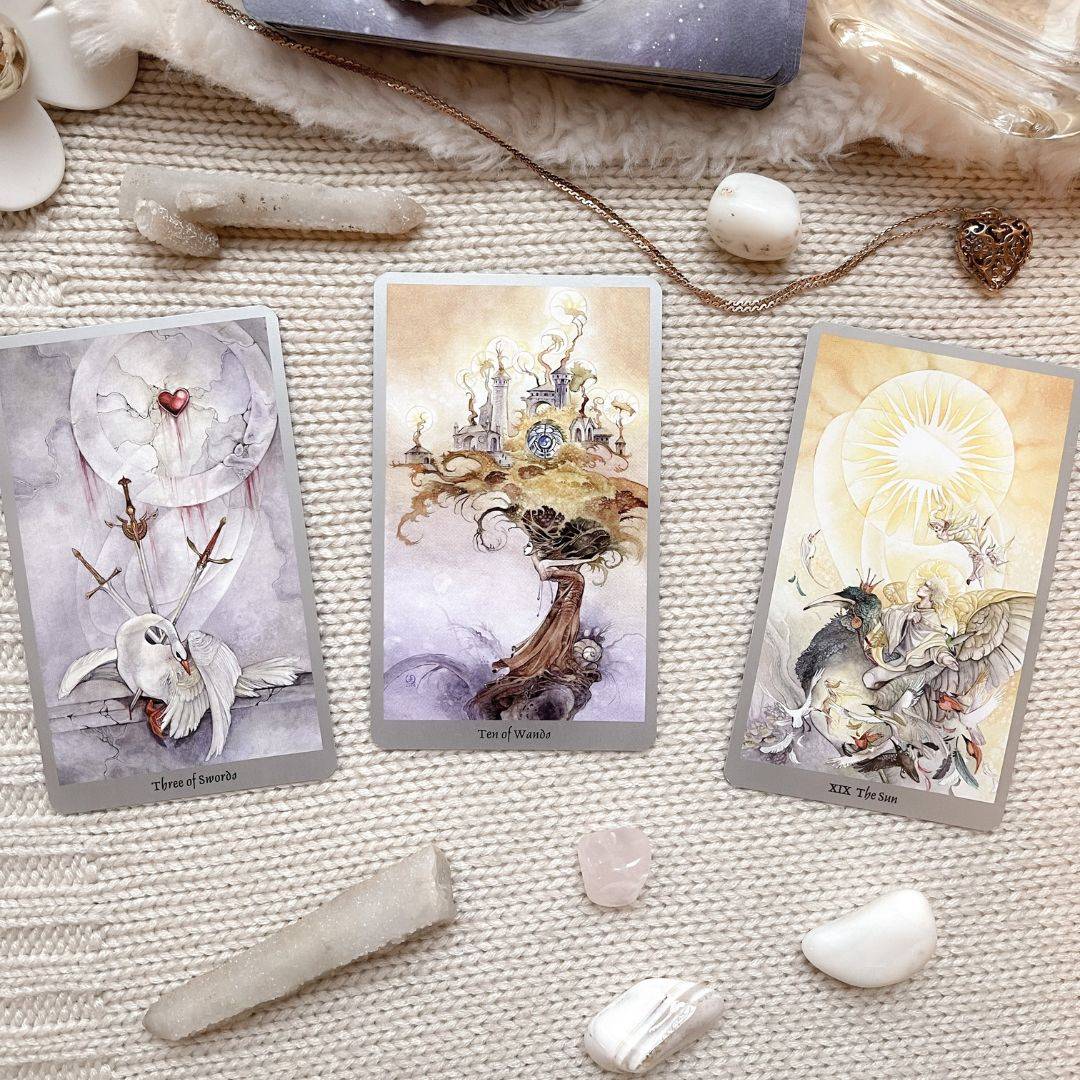 Three tarot cards surrounded by crystals and a pendulum