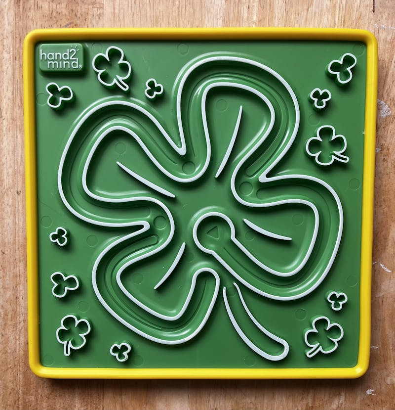 Green, square maze of a four leaf clover. The walls of the maze are raised. There is an indented triangle to mark the start and there are indented circles to mark where to hold your breath.