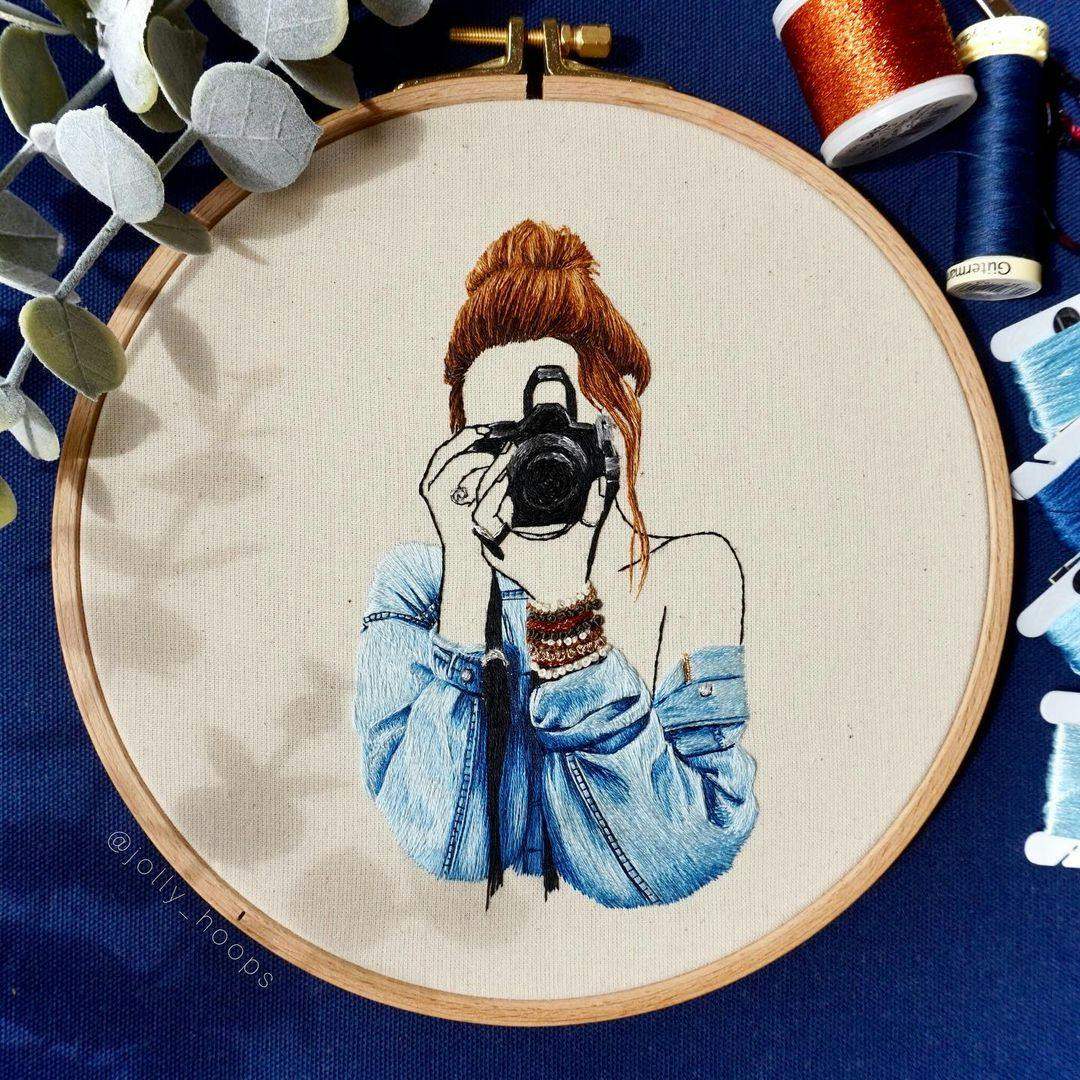 Embroidery of a person holding a camera up to their face