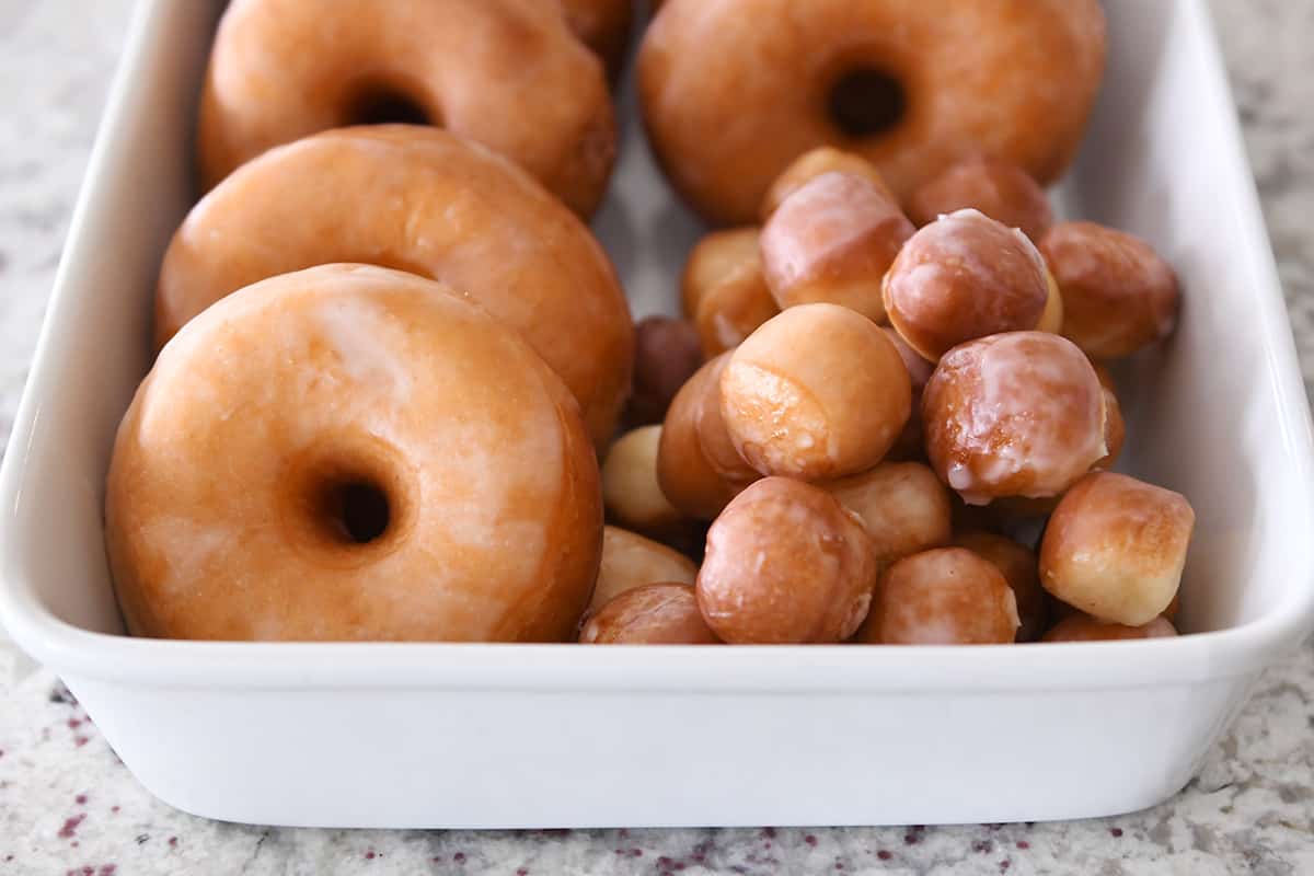A white dish filled with glazed donuts and donut holes on a speckled countertop.