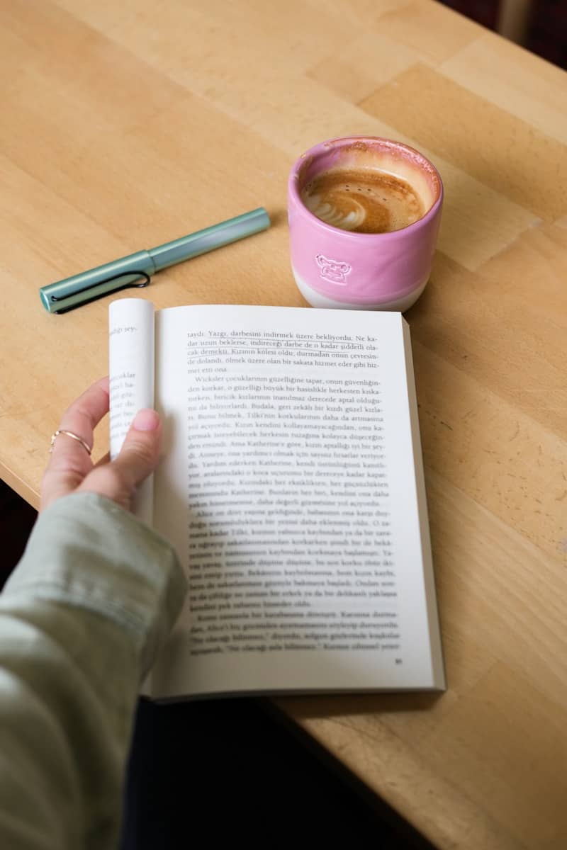 Person reading a book with coffee and pen.