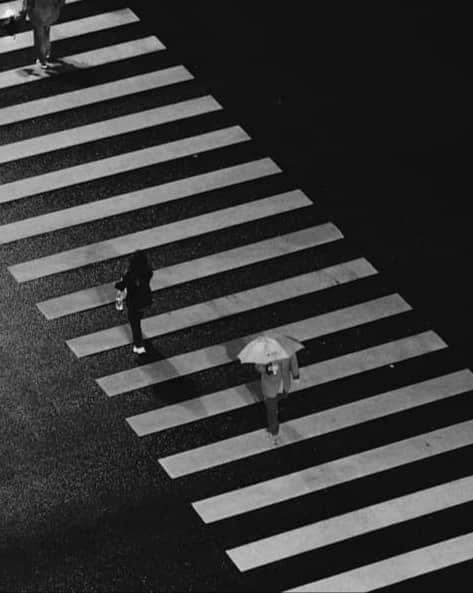 People crossing a wet zebra crossing at night.