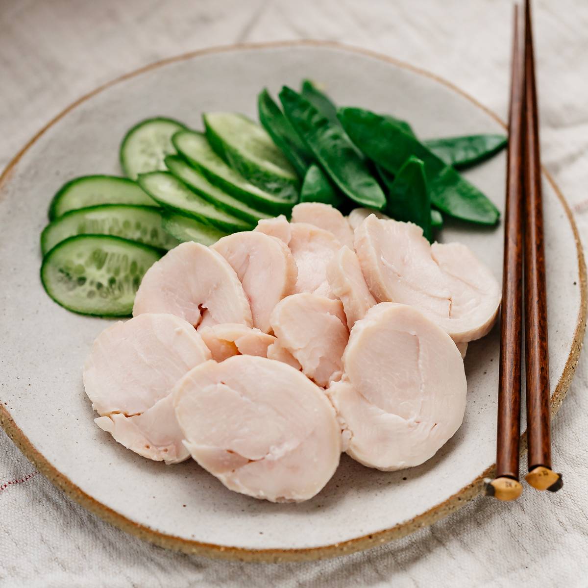 Sliced chicken ham served on a flat round plate with slices of cucumber