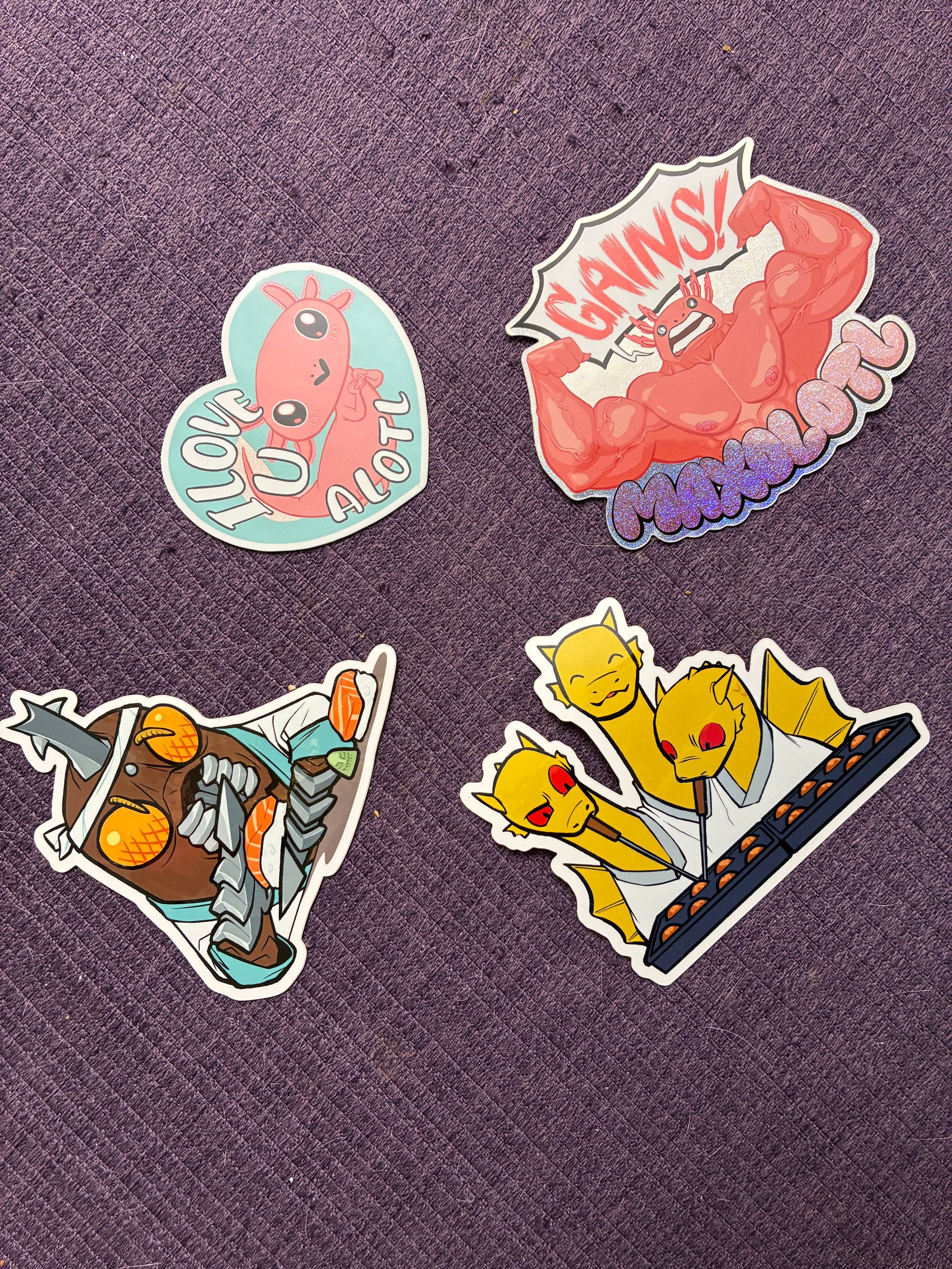 Four stickers. Top left is an axolotly making heart fingers with the text "I Love U Alotl." Top right is an axolotl flexing yelling GAINS with the word "Maxolotl" below. On the bottom left is Megalon dressed as a sushi chef. On the bottom right is King Ghidora dressed as a takoyaki 