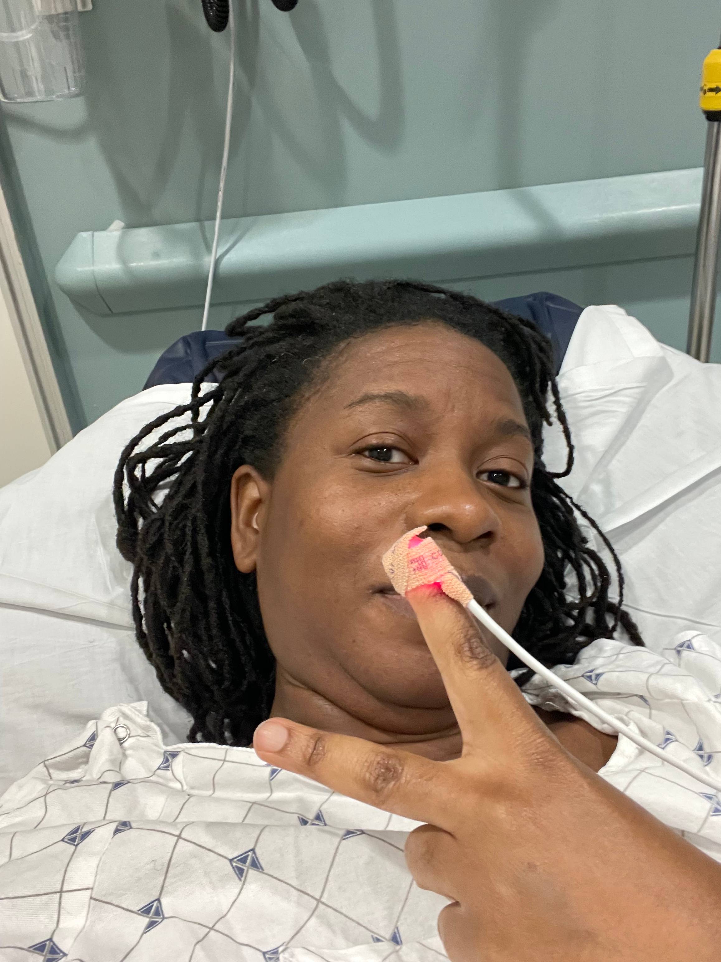 Picture of Kiante in the hospital bed with gown being positive holding up a peace sign.