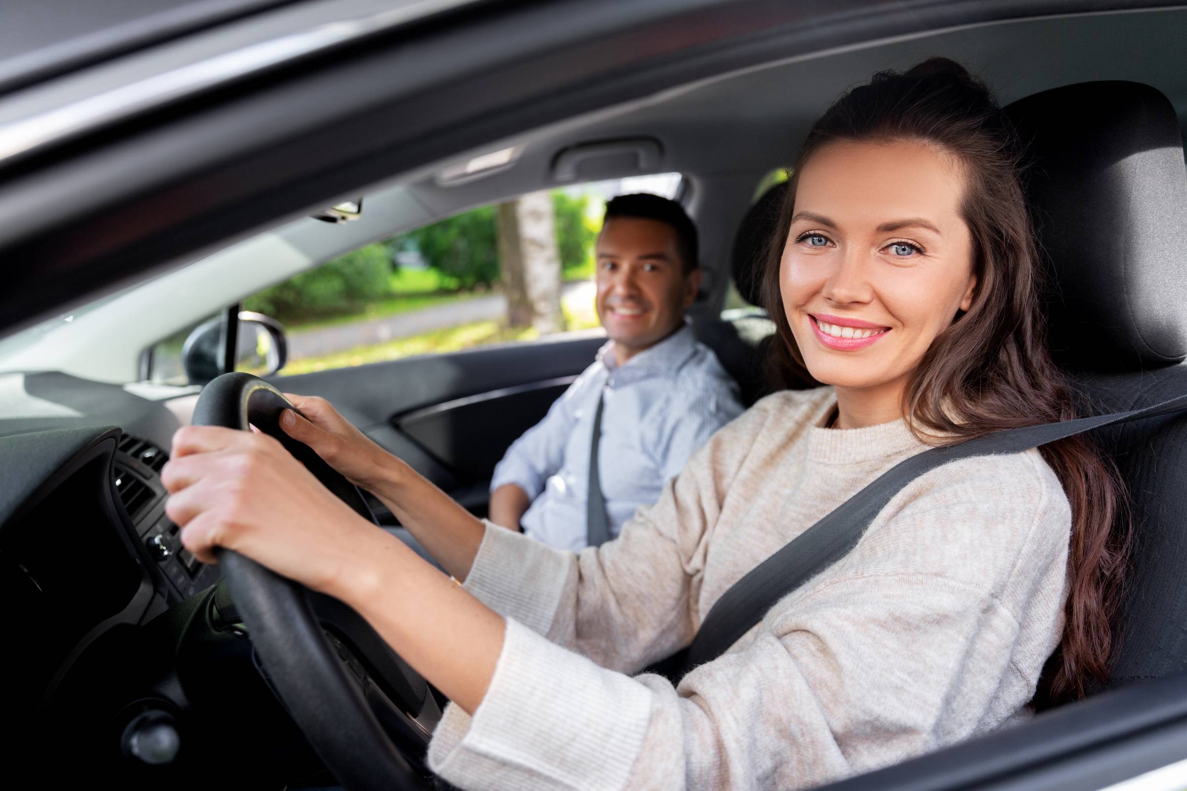 driver courses and people concept - car driving school instructor teaching young woman to drive