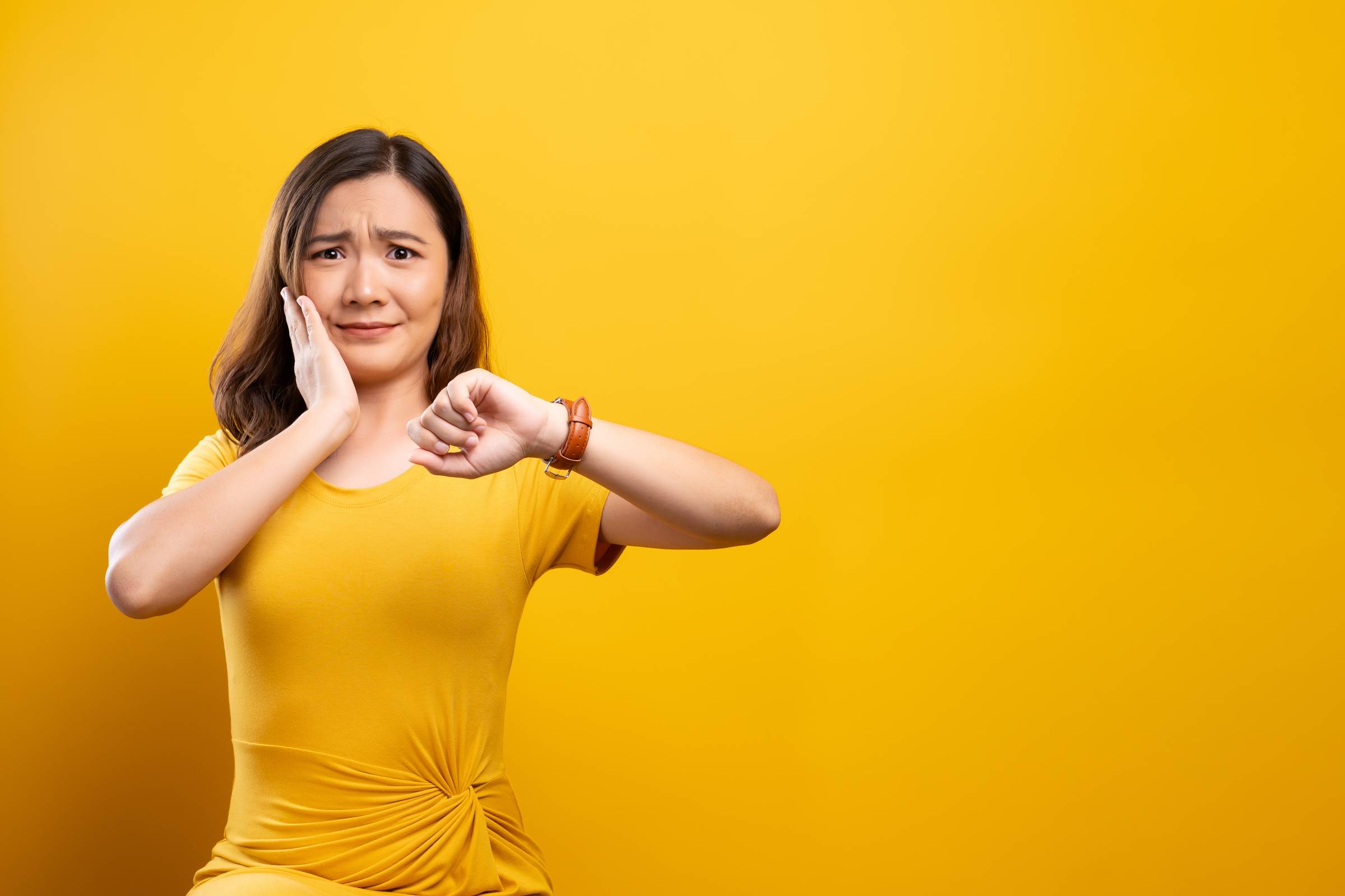 Shocked woman holding hand with wrist watch isolated on a yellow background