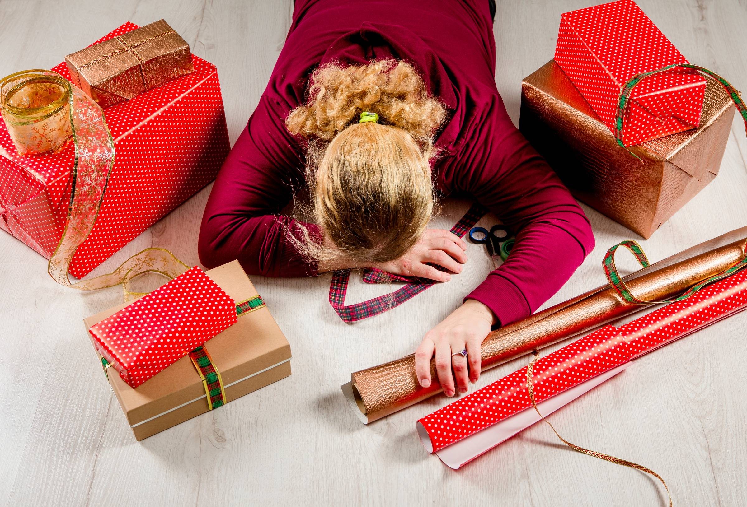 Top down view of unrecognizable woman housewife tired of wrapping Christmas presents and lying down. Seasonal holidays depression concept.