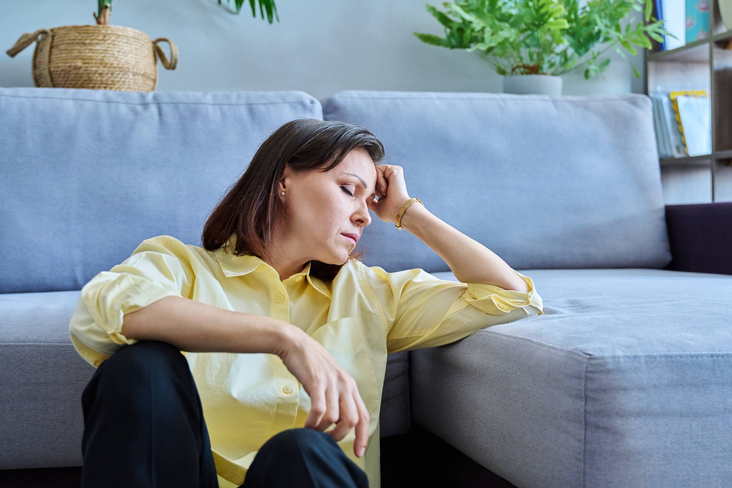 Sad upset middle-aged woman sitting on the floor near the sofa