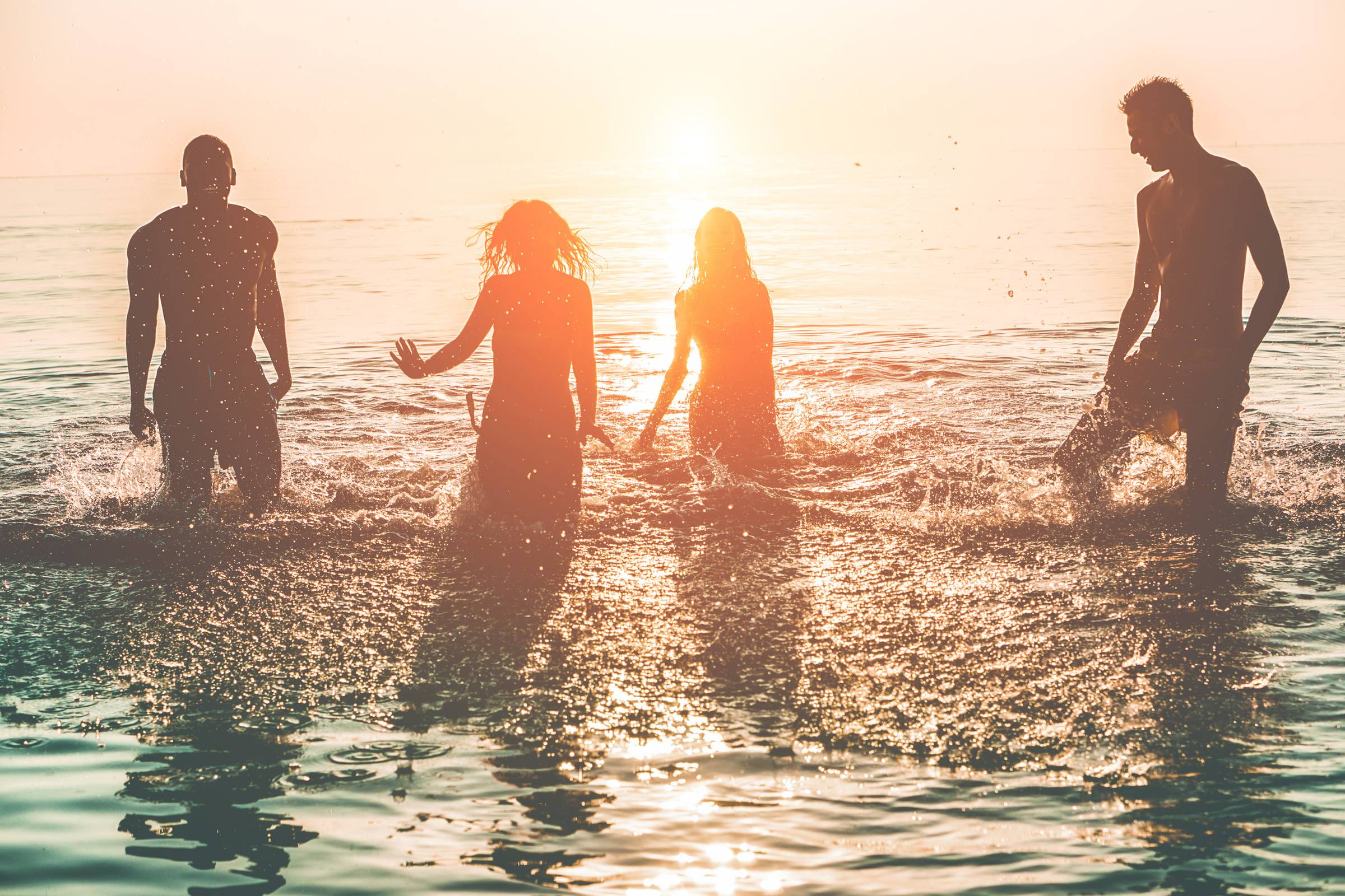 Happy friends swimming on tropical beach at sunset - Group of young people having fun on summer vacation - Youth lifestyle, party and friendship concept - Focus on bodies