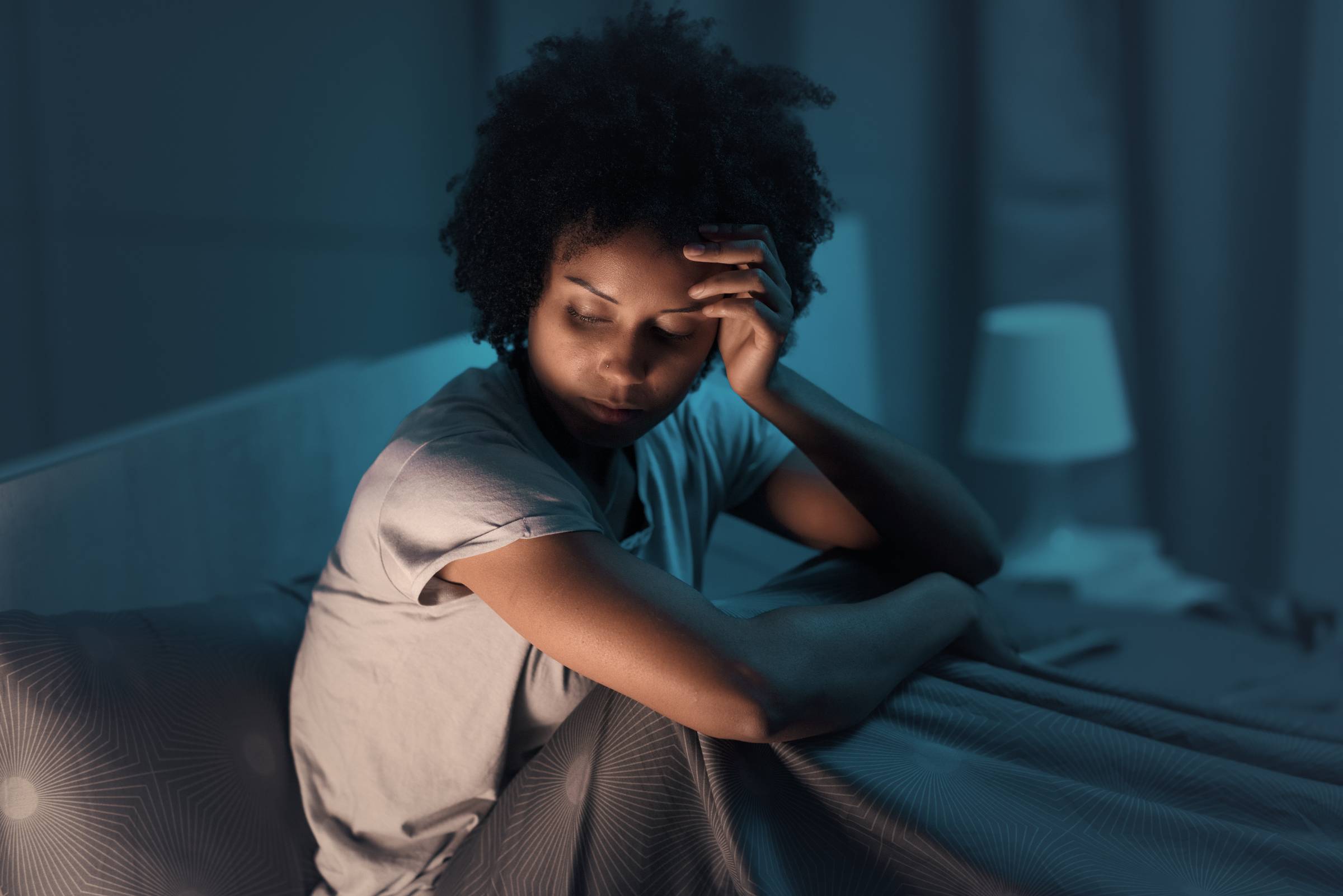 Parent awake at night worried about something sitting in the bed with hand on her head.
