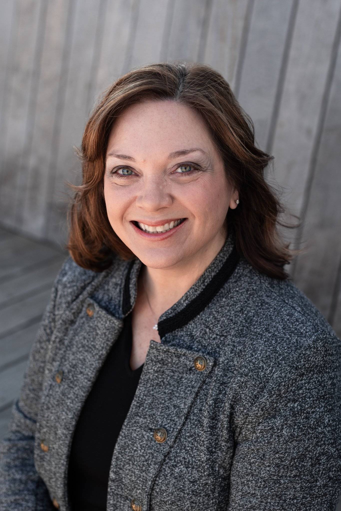 Rose's headshot. She smiles at the camera, wearing a grey blazer and black top.