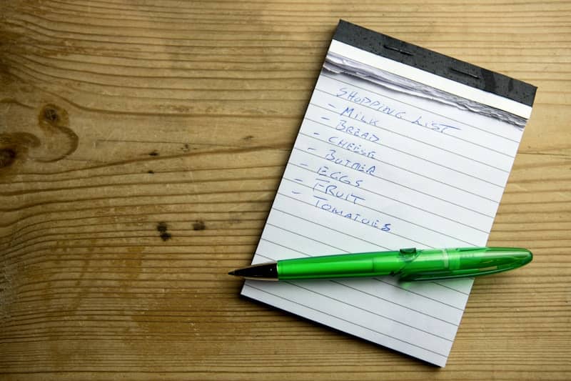 a notepad with a grocery list and a green pen on top of it