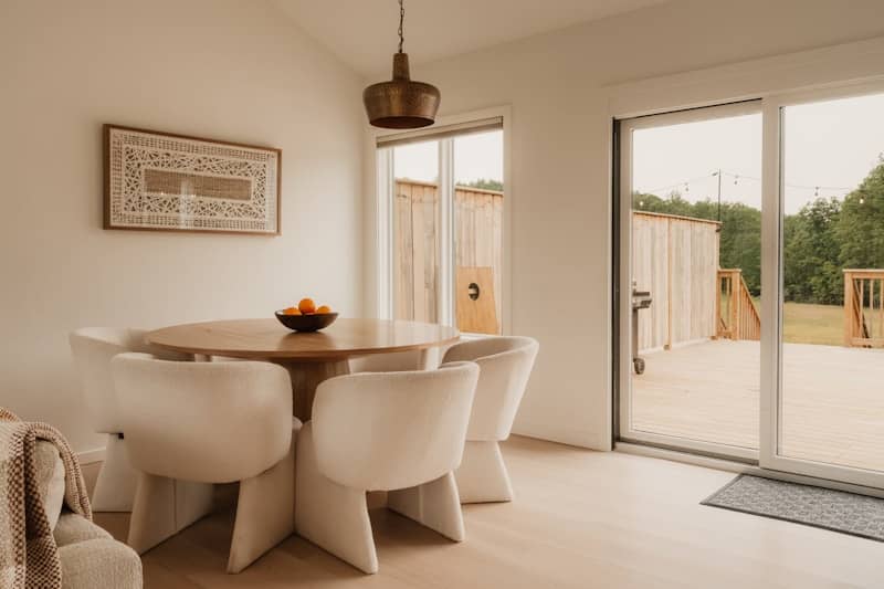 A round wooden dining table with white chairs in a bright modern room