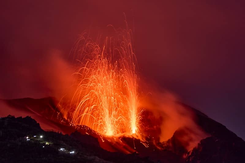 Volcano erupting with glowing lava and smoke at night.