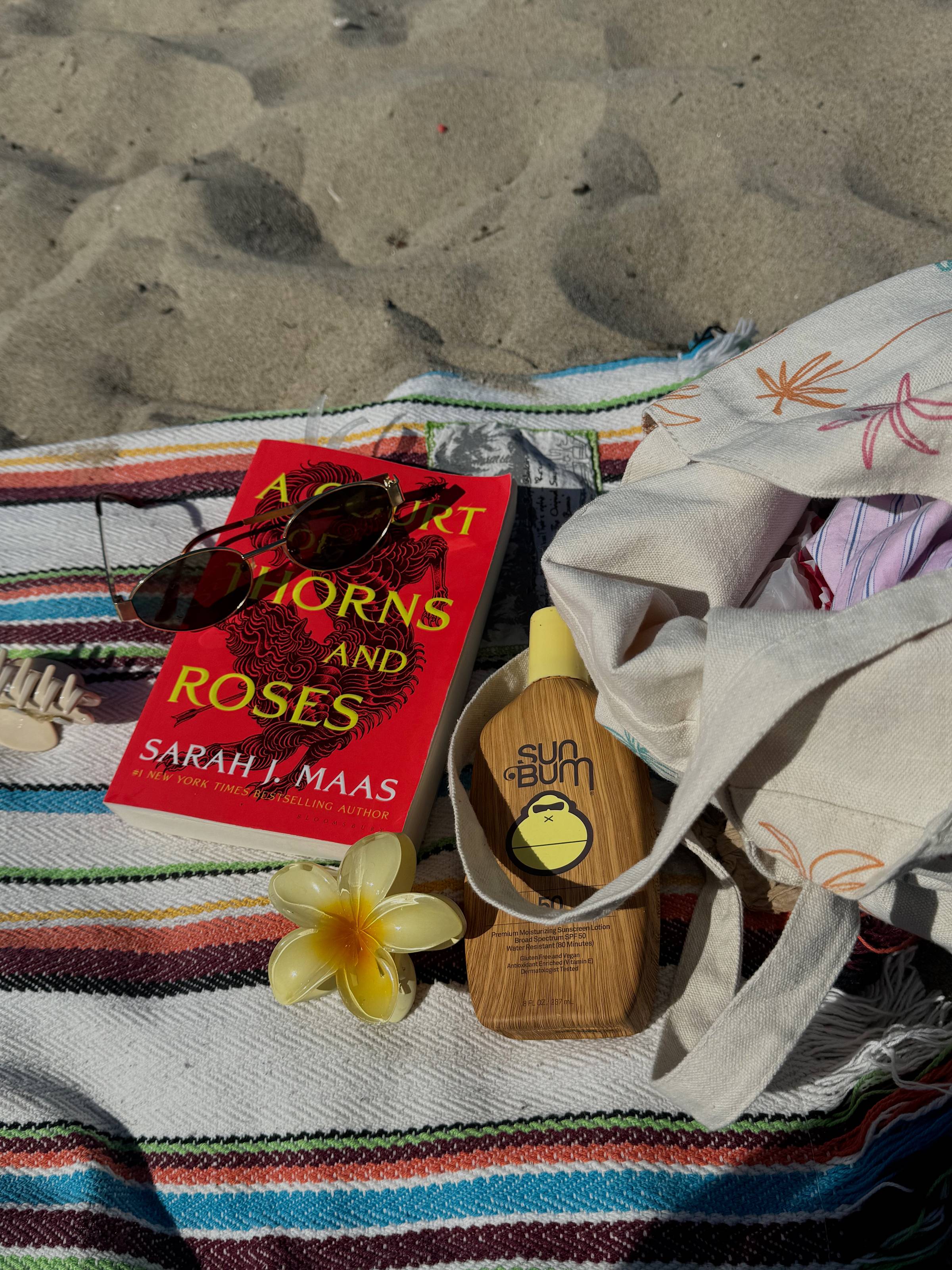 Image of ACOTAR and sun bum on a beach towel on sand