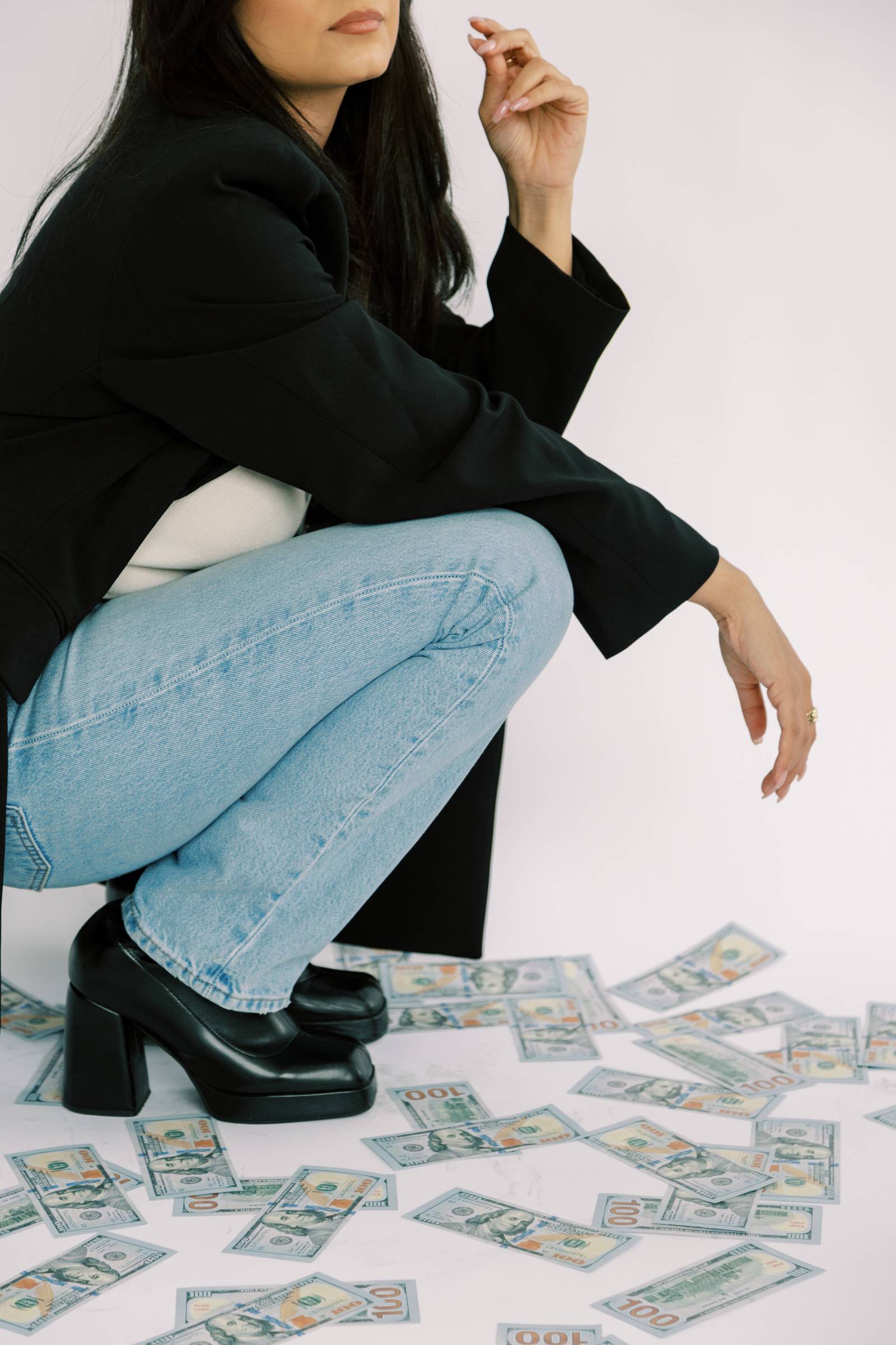 Image of a women kneeling wearing jeans and a black blazer with money surrounding her