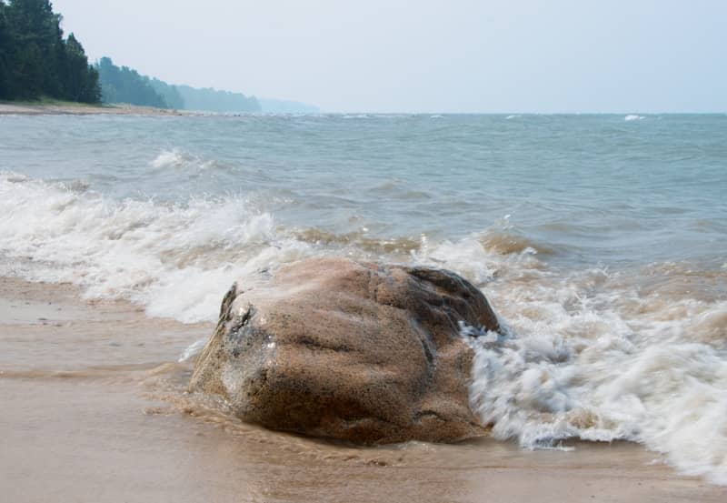 Waves crashing over a large rock on a sandy shore.