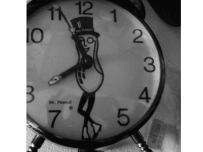 Clock with, in the center, a peanut with a face and legs wearing a black top hat.