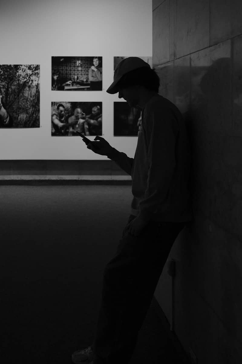 Person in hat looks at phone near wall art