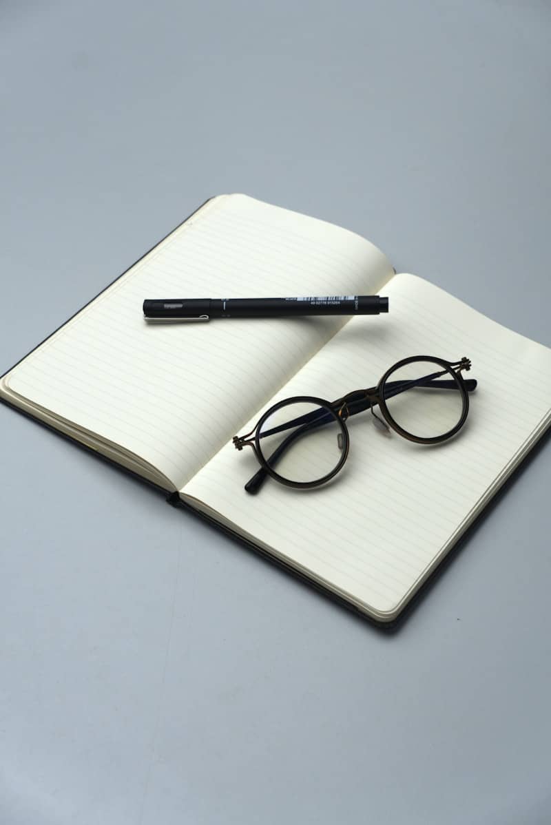 A black pen and glasses rest on an open notebook.