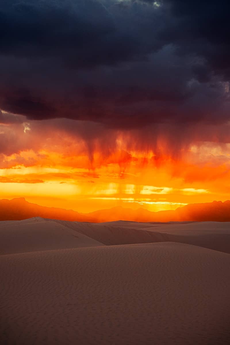 Dramatic sunset over sand dunes with rain falling.