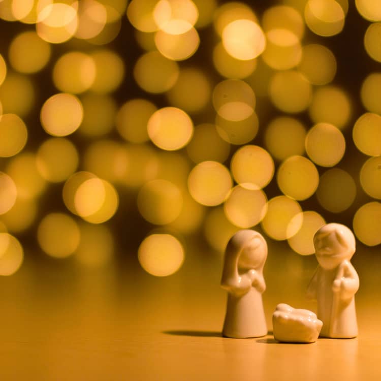 3 little figures: Mary, Joseph and baby Jesus in front of an array of lights