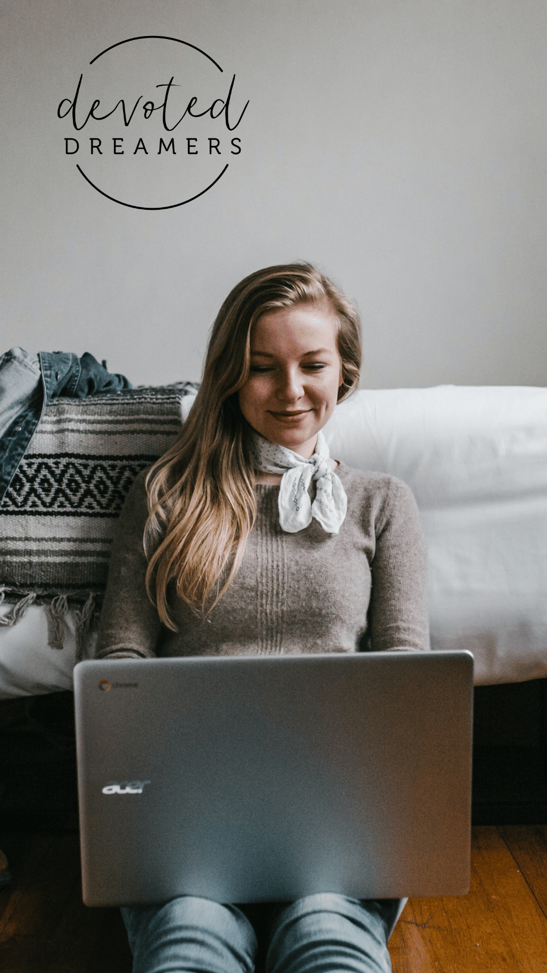 woman sitting beside a bed while using a laptop