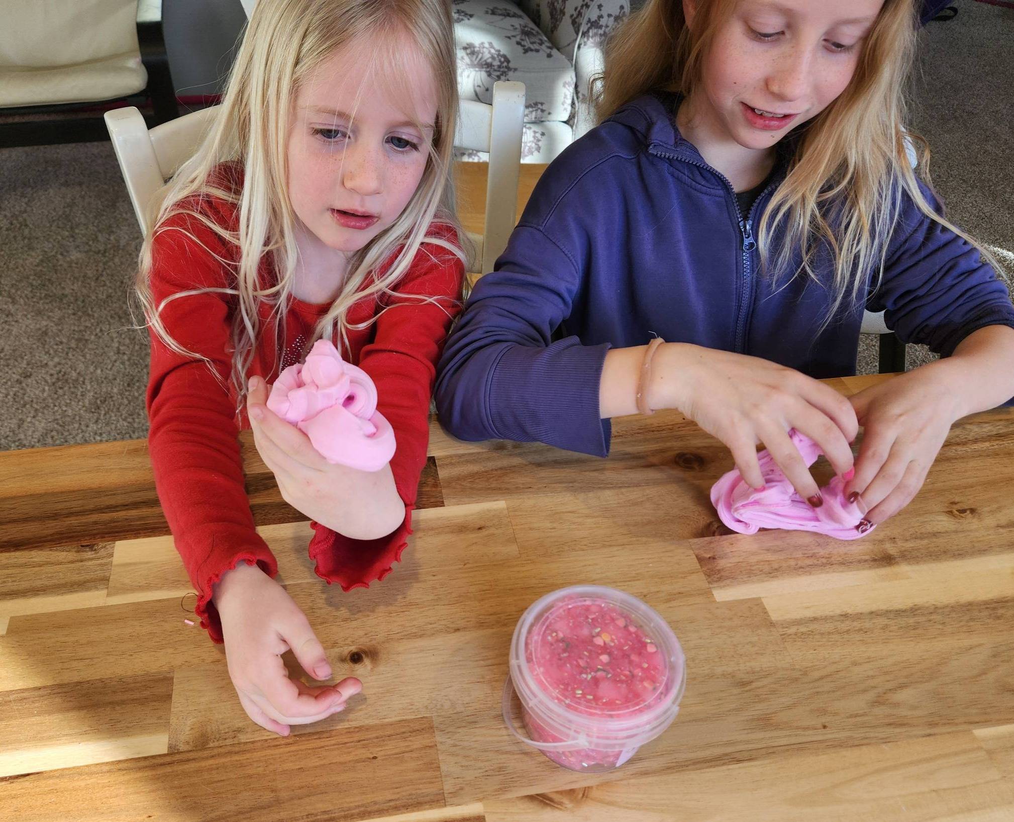 two girls playing with pink slime on a wooden table
