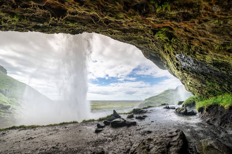 View from behind a waterfall into a green landscape.