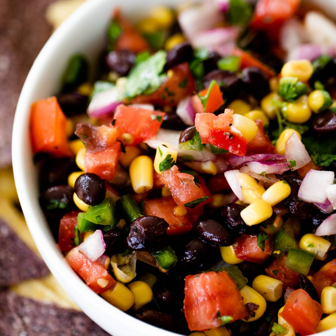 black beans, tomatoes, corn, onion and cilantro sit mixed together in a bowl