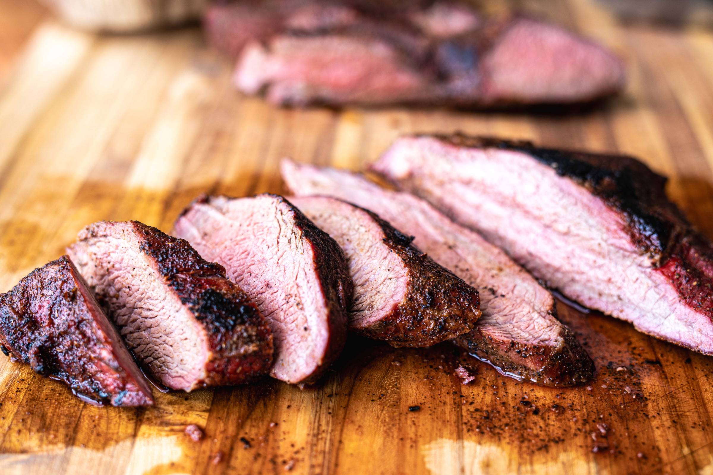 tri tip steak is sliced and resting on wooden cutting board