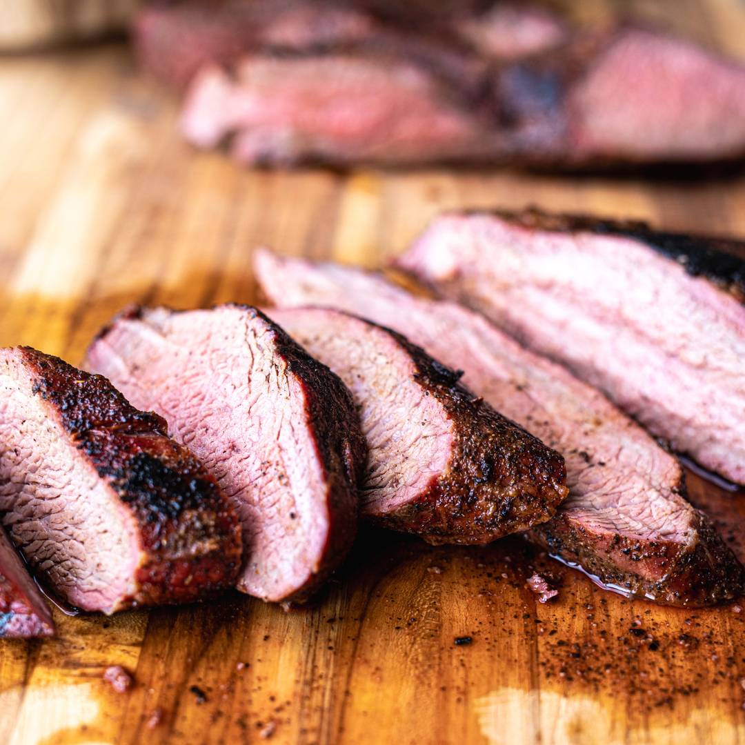 sliced tri tip steak rests on a wooden cutting board